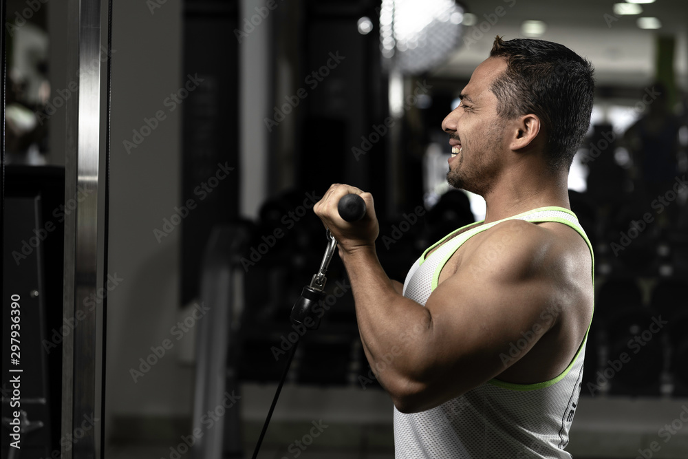 Young latin man at gym working  biceps extension with dumbbells and pulley 