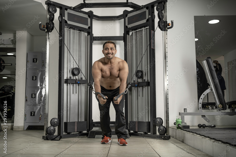 Naklejka premium Young latin man at gym working triceps, chest, back, arms with pulley