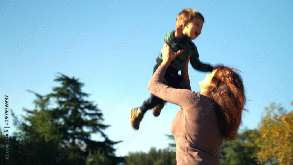 A young mother with a two year old son walks in the city. Sunny warm day in the fall. Mom throws her son up, the son rejoices and laughs. A young mother with a two year old son walks in the city. Sunny warm day in the fall. Mom throws her son up, the son rejoices and laughs.