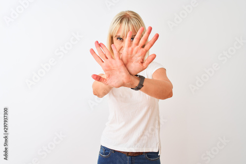 Middle age woman wearing casual t-shirt standing over isolated white background Rejection expression crossing arms and palms doing negative sign, angry face