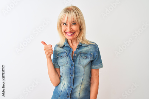 Middle age woman wearing casual denim shirt standing over isolated white background doing happy thumbs up gesture with hand. Approving expression looking at the camera showing success.
