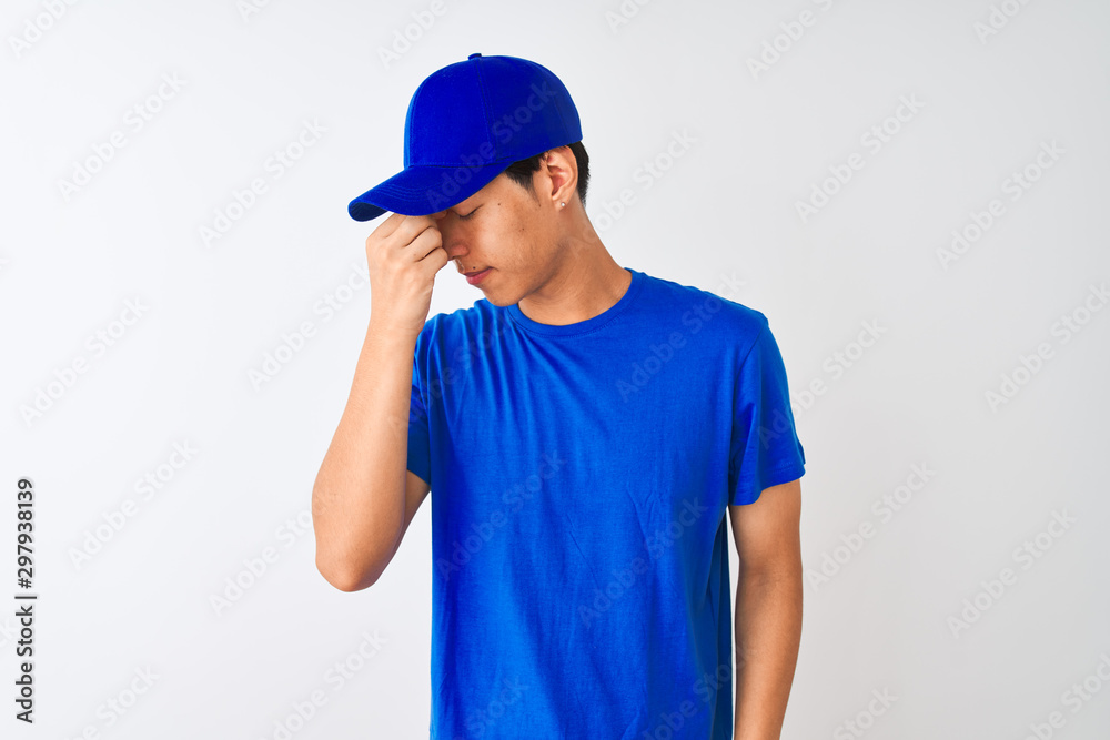 Chinese deliveryman wearing blue t-shirt and cap standing over isolated white background tired rubbing nose and eyes feeling fatigue and headache. Stress and frustration concept.