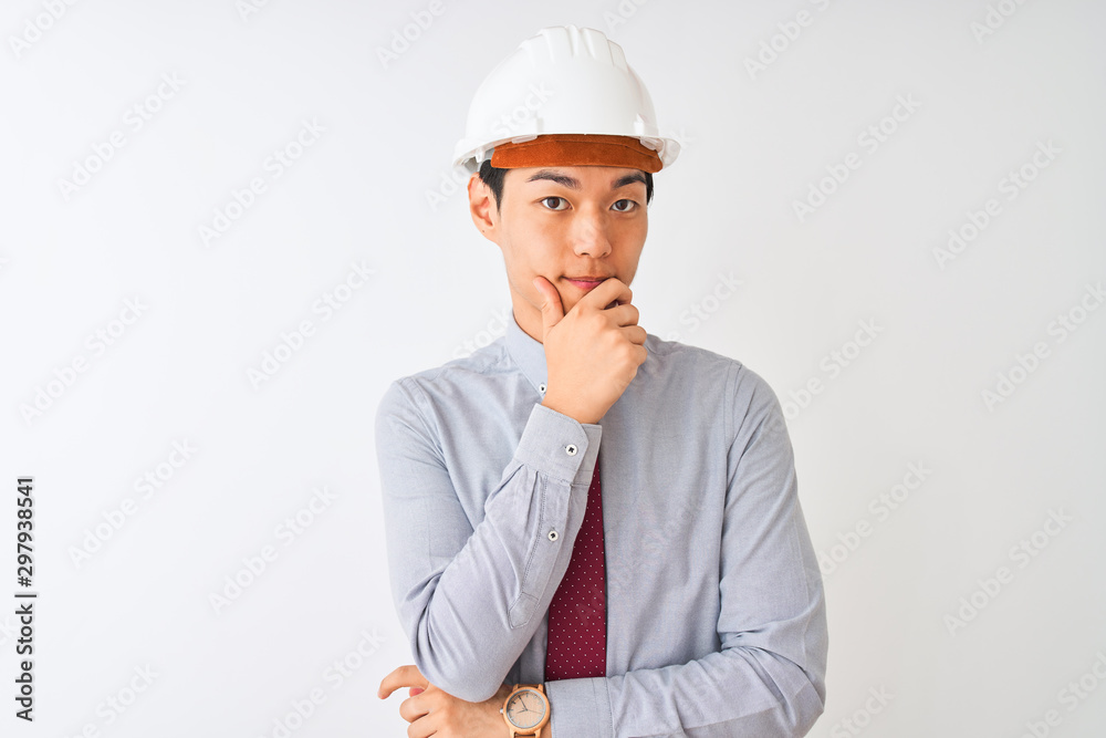 Chinese architect man wearing tie and helmet standing over isolated white background looking confident at the camera with smile with crossed arms and hand raised on chin. Thinking positive. Chinese architect man wearing tie and helmet standing over isolated white background looking confident at the camera with smile with crossed arms and hand raised on chin. Thinking positive.