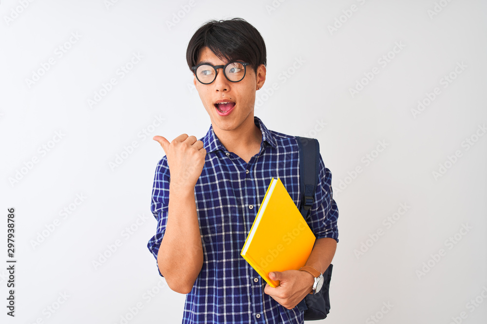 Chinese student man wearing backpack holding notebook over isolated white background pointing and showing with thumb up to the side with happy face smiling Chinese student man wearing backpack holding notebook over isolated white background pointing and showing with thumb up to the side with happy face smiling