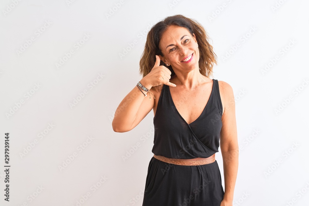 Middle age woman wearing black casual dress standing over isolated white background smiling doing phone gesture with hand and fingers like talking on the telephone. Communicating concepts. Middle age woman wearing black casual dress standing over isolated white background smiling doing phone gesture with hand and fingers like talking on the telephone. Communicating concepts.