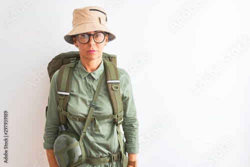 Middle age hiker woman wearing backpack canteen hat glasses over isolated white background Relaxed with serious expression on face. Simple and natural looking at the camera.