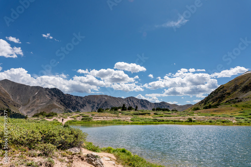 Fototapeta Naklejka Na Ścianę i Meble -  A beautiful mountain landscape with a lake surrounded by rocky mountains, and a bright blue sky with puffy clouds