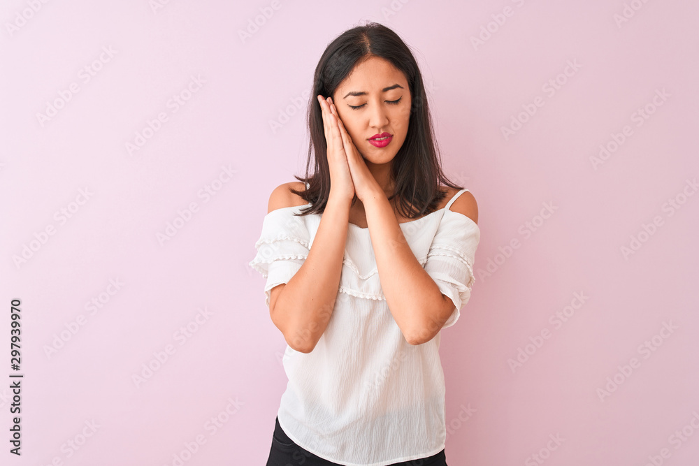 Beautiful chinese woman wearing white t-shirt standing over isolated pink background sleeping tired dreaming and posing with hands together while smiling with closed eyes. Beautiful chinese woman wearing white t-shirt standing over isolated pink background sleeping tired dreaming and posing with hands together while smiling with closed eyes.