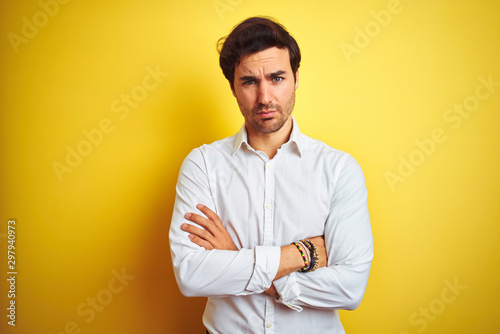 Young handsome businessman wearing elegant shirt standing over isolated yellow background skeptic and nervous, disapproving expression on face with crossed arms. Negative person.