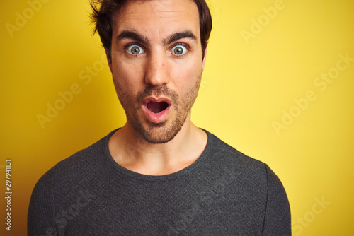 Young handsome man wearing casual sweater standing over isolated yellow background scared in shock with a surprise face, afraid and excited with fear expression © Krakenimages.com