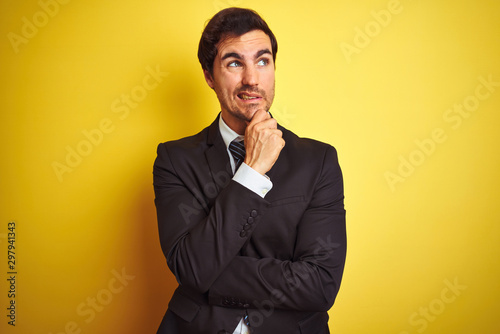 Young handsome businessman wearing suit and tie standing over isolated yellow background Thinking worried about a question, concerned and nervous with hand on chin