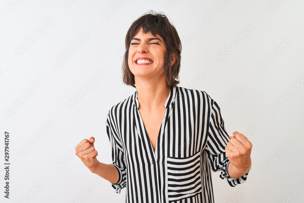 Young beautiful woman wearing striped shirt standing over isolated white background very happy and excited doing winner gesture with arms raised, smiling and screaming for success. Celebration concept Young beautiful woman wearing striped shirt standing over isolated white background very happy and excited doing winner gesture with arms raised, smiling and screaming for success. Celebration concept