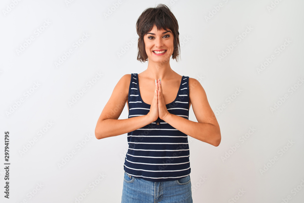 Young beautiful woman wearing striped t-shirt standing over isolated white background praying with hands together asking for forgiveness smiling confident. Young beautiful woman wearing striped t-shirt standing over isolated white background praying with hands together asking for forgiveness smiling confident.
