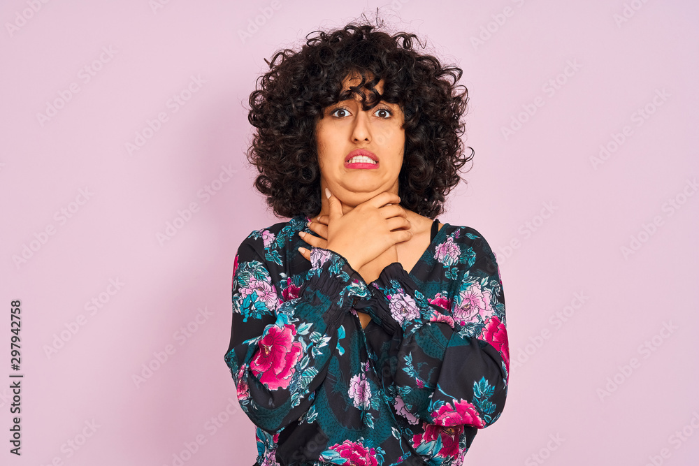 Young arab woman with curly hair wearing floral dress over isolated pink background shouting and suffocate because painful strangle. Health problem. Asphyxiate and suicide concept. Young arab woman with curly hair wearing floral dress over isolated pink background shouting and suffocate because painful strangle. Health problem. Asphyxiate and suicide concept.