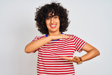 Young arab woman with curly hair wearing striped t-shirt over isolated white background gesturing with hands showing big and large size sign, measure symbol. Smiling looking at the camera.