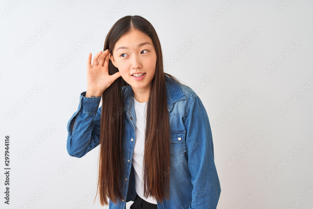 Young chinese woman wearing denim shirt standing over isolated white background smiling with hand over ear listening an hearing to rumor or gossip. Deafness concept. Young chinese woman wearing denim shirt standing over isolated white background smiling with hand over ear listening an hearing to rumor or gossip. Deafness concept.