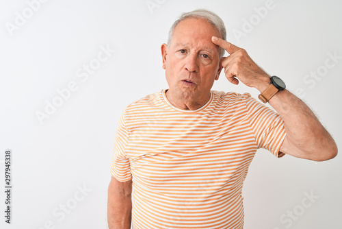 Senior grey-haired man wearing striped t-shirt standing over isolated white background pointing unhappy to pimple on forehead, ugly infection of blackhead. Acne and skin problem