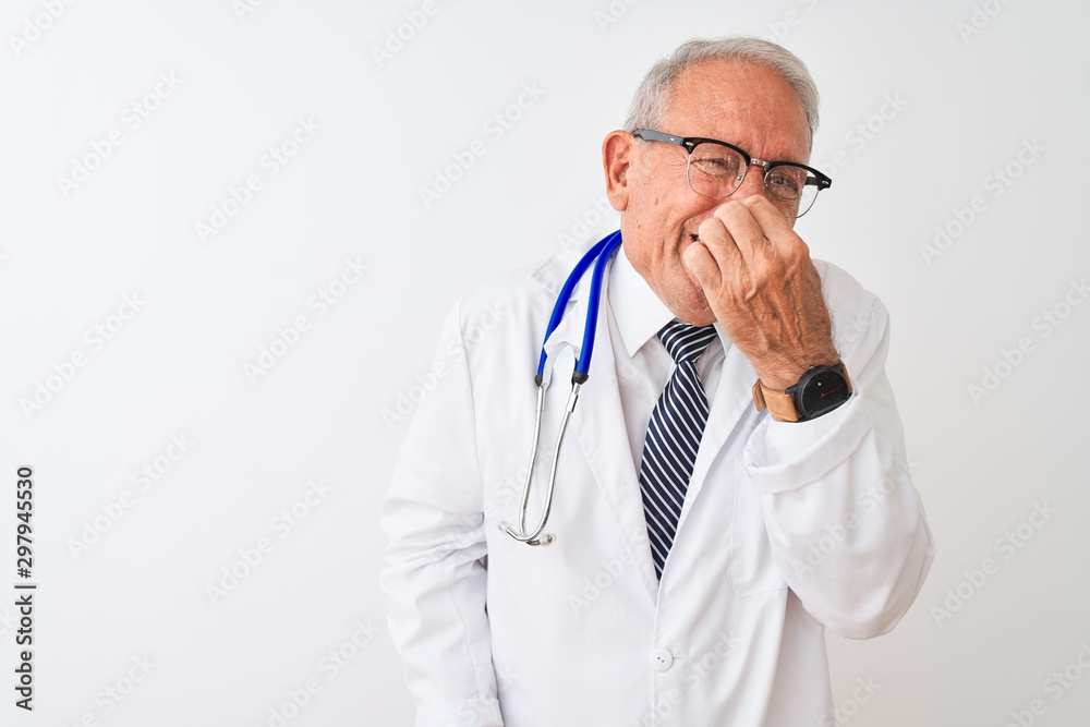 Senior grey-haired doctor man wearing stethoscope standing over isolated white background smelling something stinky and disgusting, intolerable smell, holding breath with fingers on nose. Bad smells Senior grey-haired doctor man wearing stethoscope standing over isolated white background smelling something stinky and disgusting, intolerable smell, holding breath with fingers on nose. Bad smells