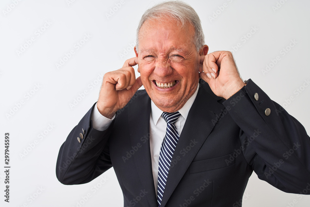 Senior grey-haired businessman wearing suit standing over isolated white background covering ears with fingers with annoyed expression for the noise of loud music. Deaf concept.