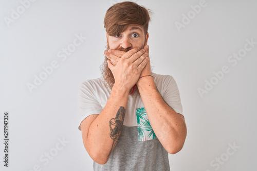 Fototapeta Naklejka Na Ścianę i Meble -  Young redhead irish man wearing t-shirt standing over isolated white background shocked covering mouth with hands for mistake. Secret concept.
