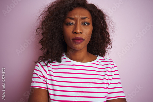 Young african american woman wearing striped t-shirt standing over isolated pink background skeptic and nervous, disapproving expression on face with crossed arms. Negative person. © Krakenimages.com