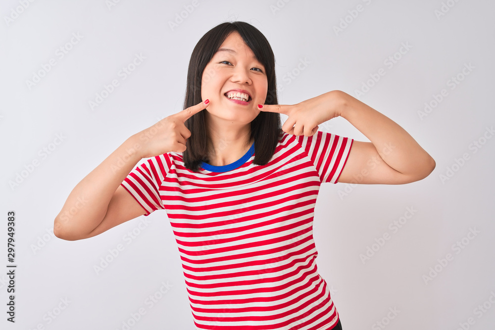 Young beautiful chinese woman wearing red striped t-shirt over isolated white background smiling cheerful showing and pointing with fingers teeth and mouth. Dental health concept. Young beautiful chinese woman wearing red striped t-shirt over isolated white background smiling cheerful showing and pointing with fingers teeth and mouth. Dental health concept.