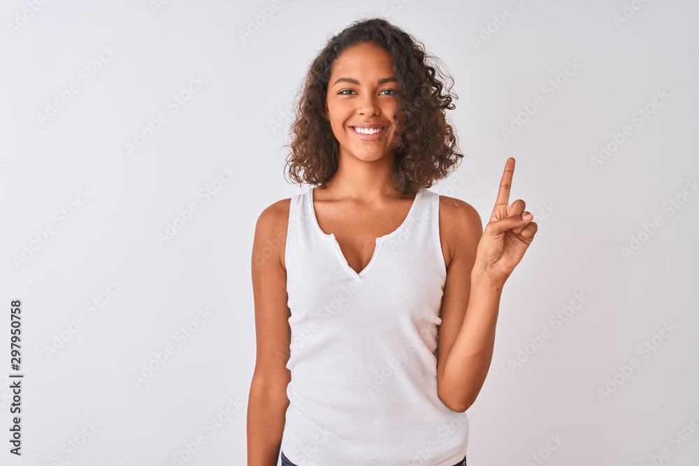 Young brazilian woman wearing casual t-shirt standing over isolated white background showing and pointing up with finger number one while smiling confident and happy. Young brazilian woman wearing casual t-shirt standing over isolated white background showing and pointing up with finger number one while smiling confident and happy.