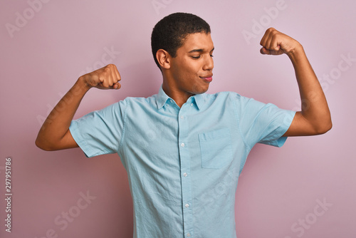 Young handsome arab man wearing blue shirt standing over isolated pink background showing arms muscles smiling proud. Fitness concept.