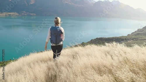 girl hiking in golden grass in New Zealand's mountains over looking blue lake photo