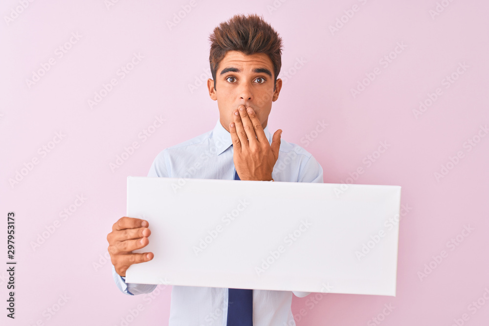 Young handsome businessman holding banner standing over isolated pink background cover mouth with hand shocked with shame for mistake, expression of fear, scared in silence, secret concept Young handsome businessman holding banner standing over isolated pink background cover mouth with hand shocked with shame for mistake, expression of fear, scared in silence, secret concept