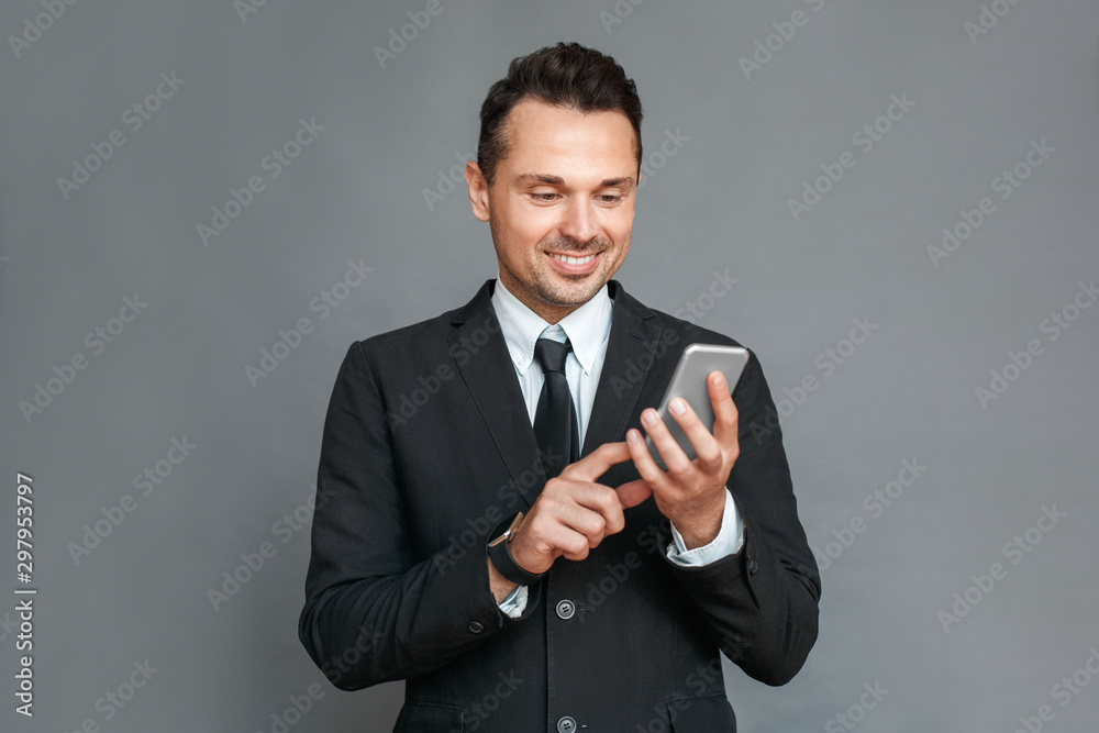 Businessman studio standing isolated on grey browsing smartphone cheerful