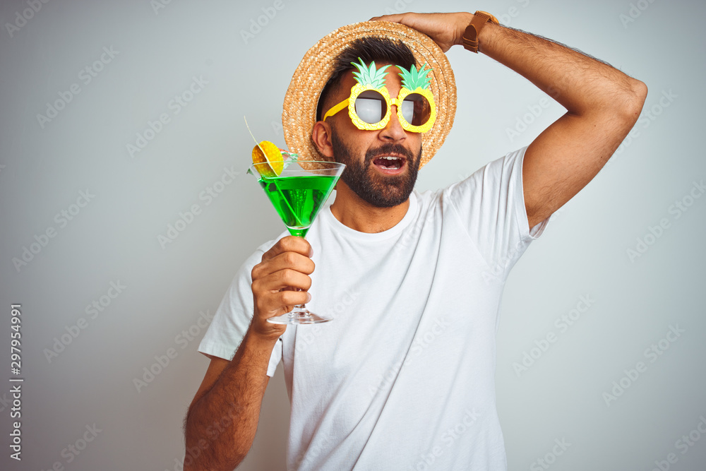 Indian man wearing summer funny look drinking cocktail over isolated white  background stressed with hand on head, shocked with shame and surprise  face, angry and frustrated. Fear and upset for mistake Stock