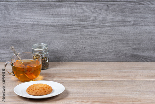 A mug of tea, a jar of tea leaves and a plate of cookies on a background of wooden boards.