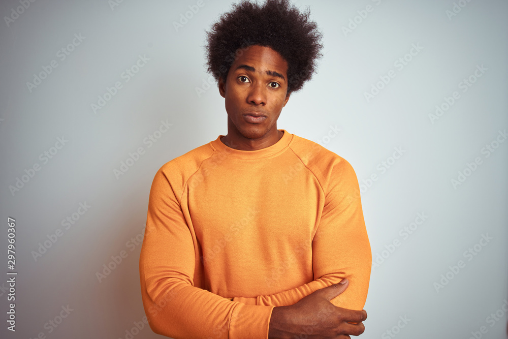 Young american man with afro hair wearing orange sweater over isolated white background skeptic and nervous, disapproving expression on face with crossed arms. Negative person. Young american man with afro hair wearing orange sweater over isolated white background skeptic and nervous, disapproving expression on face with crossed arms. Negative person.