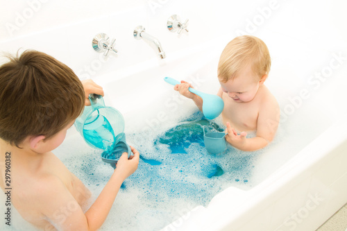 Two children playing in the bath with blue cups