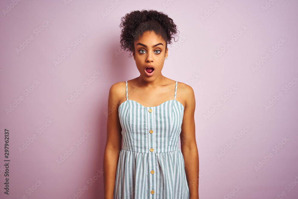 African american woman wearing casual striped dress standing over isolated pink background afraid and shocked with surprise expression, fear and excited face. African american woman wearing casual striped dress standing over isolated pink background afraid and shocked with surprise expression, fear and excited face.