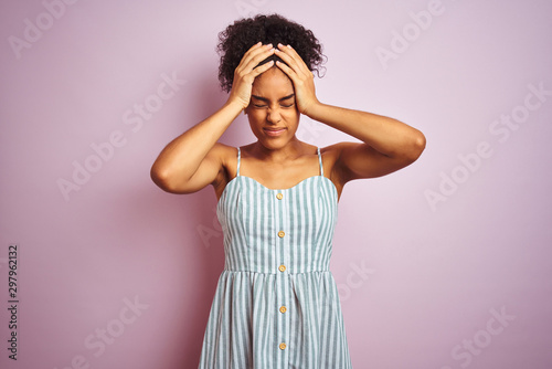 African american woman wearing casual striped dress standing over isolated pink background suffering from headache desperate and stressed because pain and migraine. Hands on head.