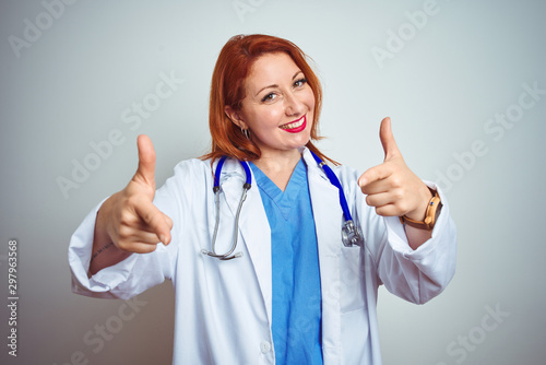 Young redhead doctor woman using stethoscope over white isolated background pointing fingers to camera with happy and funny face. Good energy and vibes.