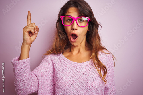 Young beautiful woman wearing fashion glasses standing over pink isolated background pointing finger up with successful idea. Exited and happy. Number one.