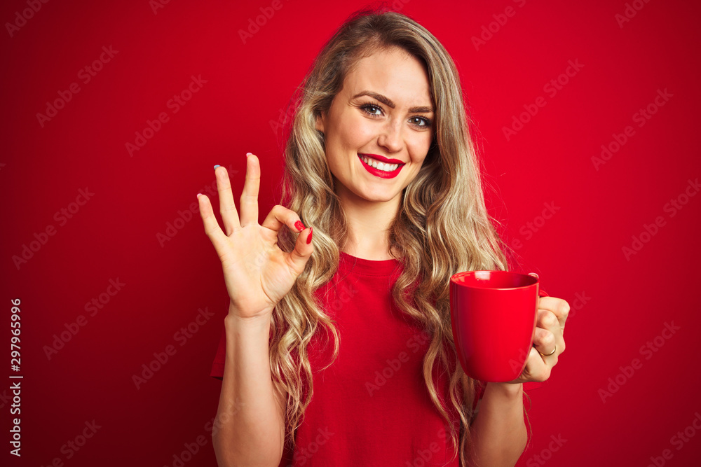 Young beautiful woman drinking a cup of cooffe over red isolated background doing ok sign with fingers, excellent symbol Young beautiful woman drinking a cup of cooffe over red isolated background doing ok sign with fingers, excellent symbol
