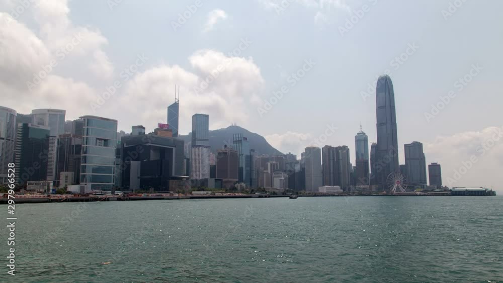Timelapse Hong Kong motorboat sails on harbor against Central and Western district with buildings and skyscrapers on bank at hill silhouette zoom out Timelapse Hong Kong motorboat sails on harbor against Central and Western district with buildings and skyscrapers on bank at hill silhouette zoom out