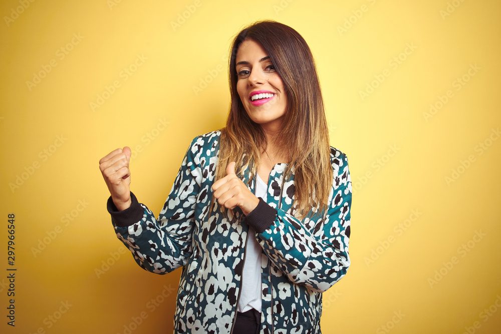 Young beautiful woman wearing casual jacket over yellow isolated background Pointing to the back behind with hand and thumbs up, smiling confident Young beautiful woman wearing casual jacket over yellow isolated background Pointing to the back behind with hand and thumbs up, smiling confident