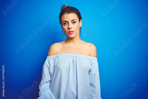 Young beautiful woman wearing bun hairstyle over blue isolated background Relaxed with serious expression on face. Simple and natural looking at the camera.