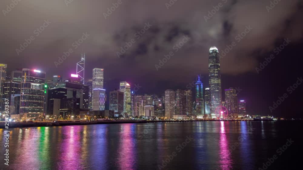 Timelapse flashing illuminated Hong Kong buildings and skyscrapers reflected in harbour water under sky with grey clouds at night zoom out Timelapse flashing illuminated Hong Kong buildings and skyscrapers reflected in harbour water under sky with grey clouds at night zoom out