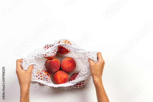 Hands holding mesh glocery shopping bag with fresh peaches on white background. Top view photo