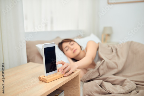 Annoying alarm. Woman lying in bed being woken by mobile phone, turning off noisy signal, closeup