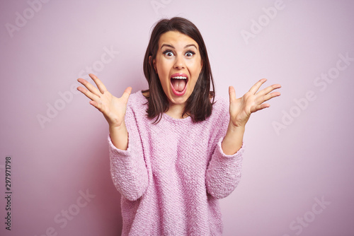 Young beautiful brunette woman wearing a sweater over pink isolated background celebrating crazy and amazed for success with arms raised and open eyes screaming excited. Winner concept