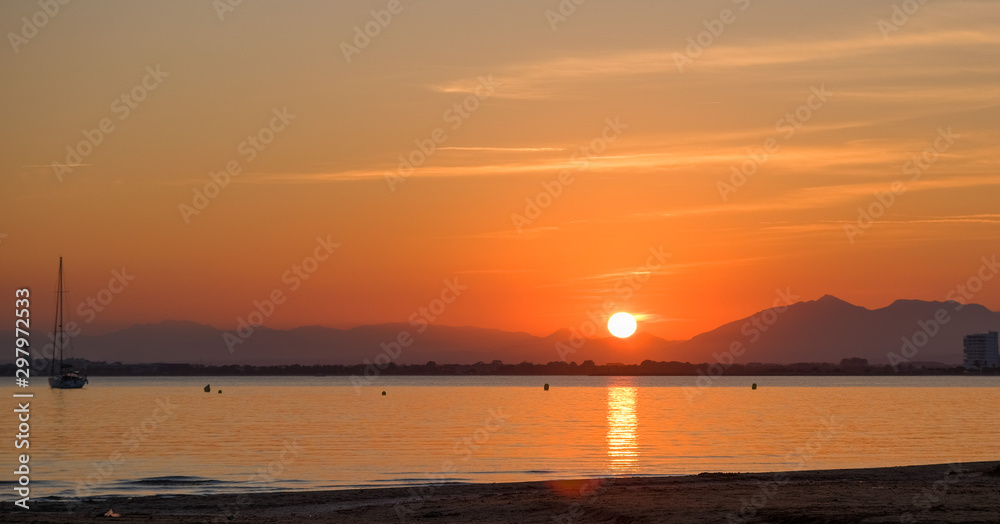 Amazing beautiful summer golden sunset over the bay of Roses, Catalunya, Spain. Sandy beach and calm sea on mountains and the evening sky background. Colorful dramatic sky above the sea.