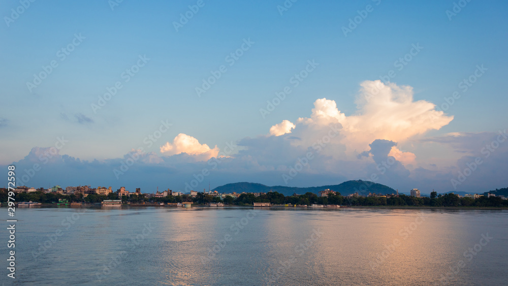 Looking at the view of a city located on the river bank with mountains and beautiful clouds in its backdrop. Guwahati city on the bank of river Brahmaputra, North East, Assam, India