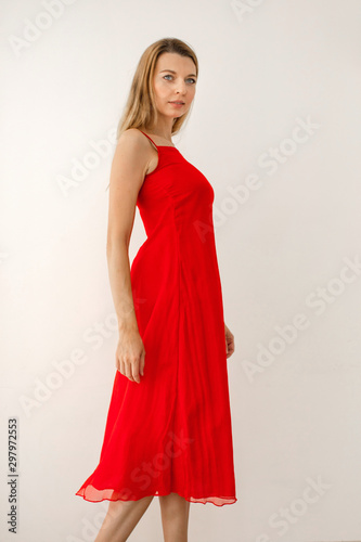 Side view of elegant confident young long haired blonde female wearing bright red midi dress with straps and open shoulders